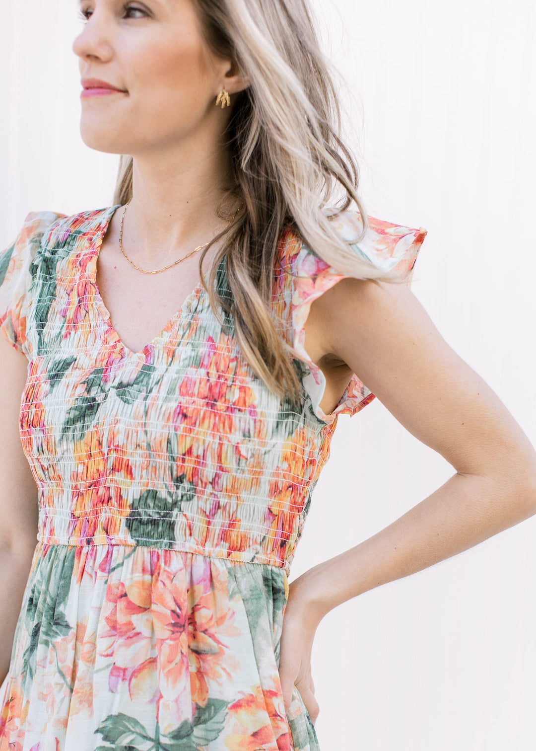 Close up of smocked bodice and flutter sleeves on a pale green v-neck dress with a floral pattern.