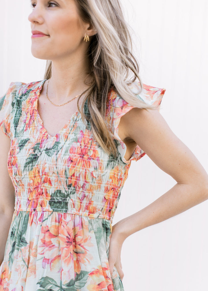 Close up of smocked bodice and flutter sleeves on a pale green v-neck dress with a floral pattern.