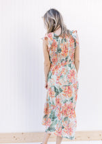 Back view of Model wearing a pale green midi with a floral pattern, smocked bodice and cap sleeves.