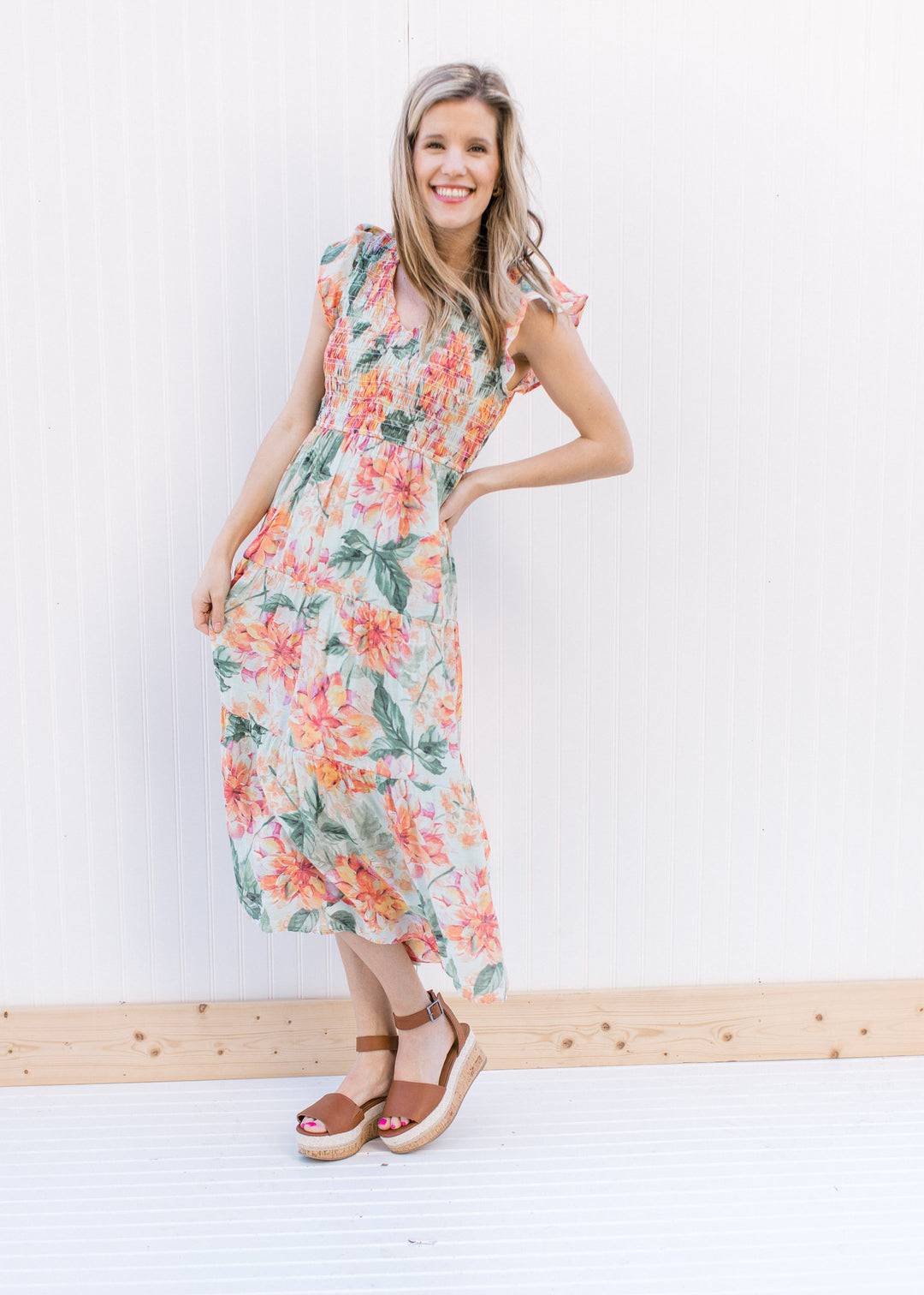 Model wearing heels with a pale green midi dress with a floral pattern and a smocked bodice.