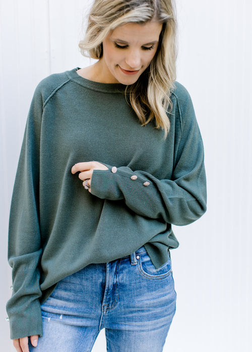 Model wearing a jade sweater with jeweled flower buttons on cuff of long sleeves and split sides. 