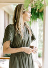 Close up of v-neck and eyelet detail on the sleeve of an olive maxi with an elastic band. 
