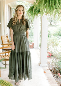 Model wearing an olive maxi with an elastic waist, pockets and eyelet detail at sleeve and hem. 