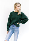 Model wearing a hunter green cable knit sweater with a polyester material and long sleeves. 