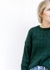 Close up of round neck and cable knit design on a hunter green sweater with long sleeves. 