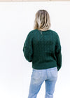 Back view of Model wearing a hunter green cable knit sweater with a crop cut and long sleeves.