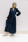 Model wearing booties with a navy tiered maxi with a v-neck and long sleeves with an elastic cuff. 