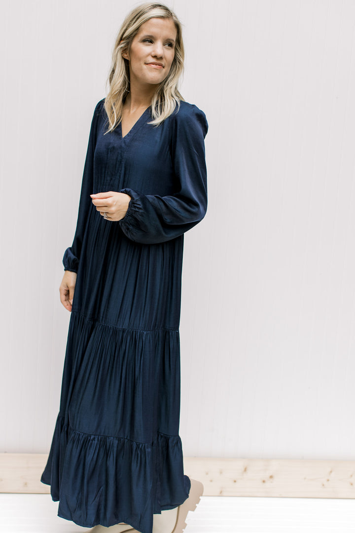 Model wearing a navy tiered maxi with a v-neck and long sleeves with an elastic cuff. 