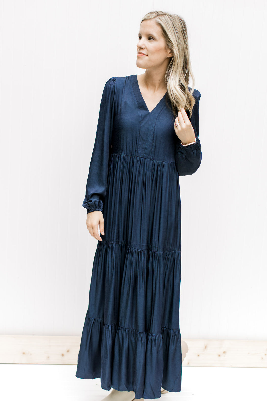 Model wearing a navy maxi with a v-neck and long sleeves with an elastic cuff and a tiered finish. 