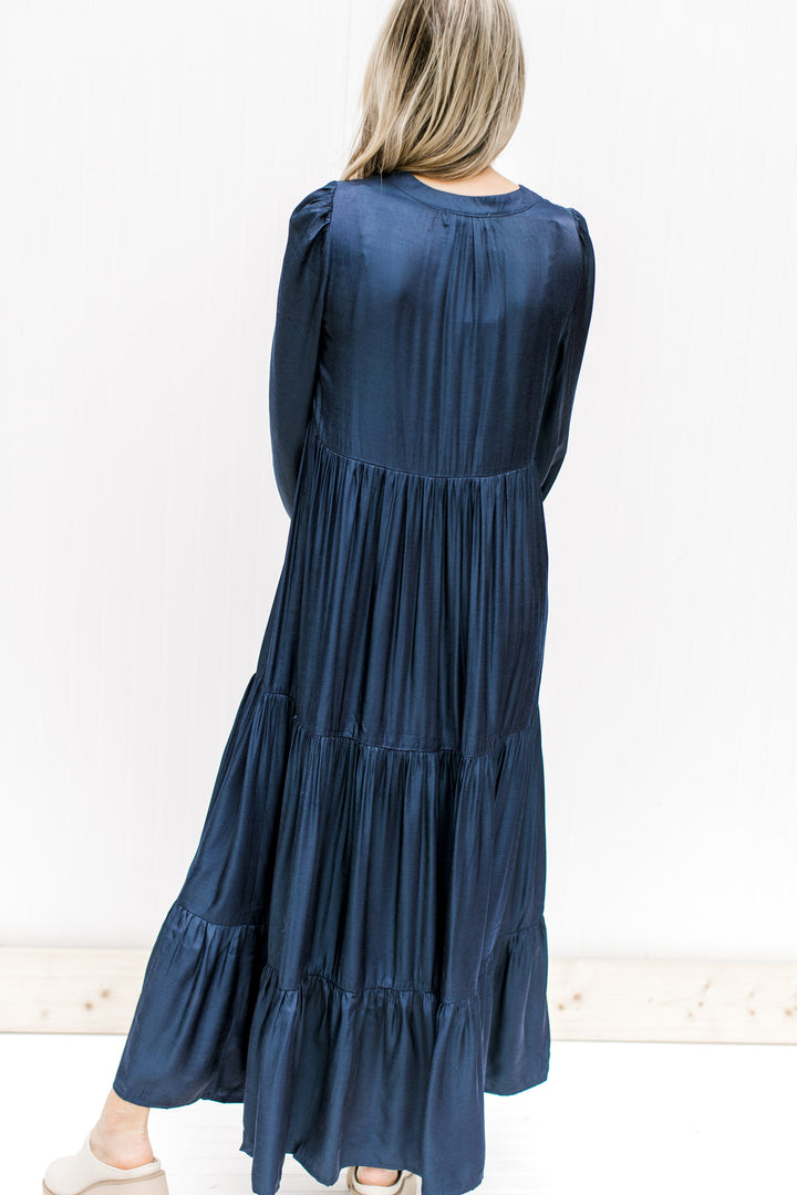 Back view of Model wearing a navy tiered maxi with a v-neck and long sleeves with an elastic cuff. 