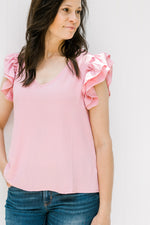 Model wearing a polyester pink v-neck top with tiered ruffle short sleeves. 