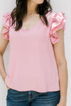 Close up of a Model wearing a polyester pink v-neck top with tiered ruffle short sleeves. 