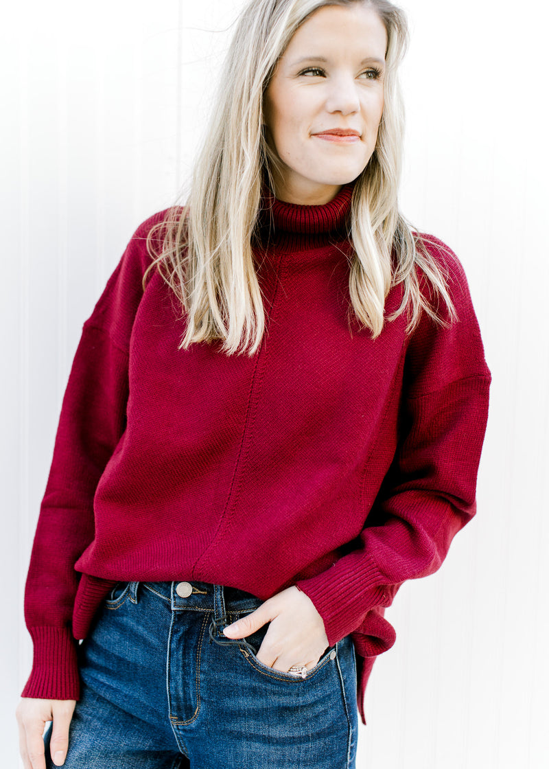 Model wearing a deep red sweater with a loose turtle neck and long sleeves. 