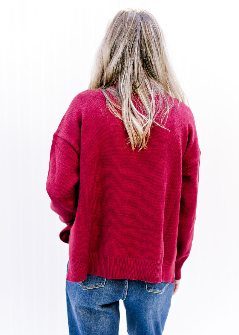 Back view of Model wearing a deep red sweater with a loose turtle neck and long sleeves. 