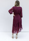 Back view of Model wearing a wine colored wrap dress with sheer 3/4 sleeves and a pleated material. 