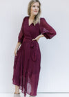 Model wearing a wine colored wrap dress with a belt, sheer 3/4 sleeves and a pleated material. 