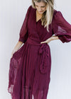 Model wearing a wine colored wrap dress with a v-neck, sheer 3/4 sleeves and a sheer overlay.