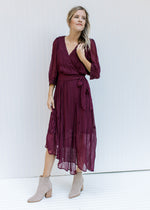 Model wearing booties with a wine colored wrap dress with sheer 3/4 sleeves and a pleated material. 
