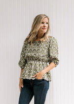 Model wearing jeans with a sage babydoll top with white embroidery, 3/4 sleeves and a square neck.