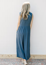 Back view of Model wearing a navy sleeveless jumpsuit with pockets and wide legs.