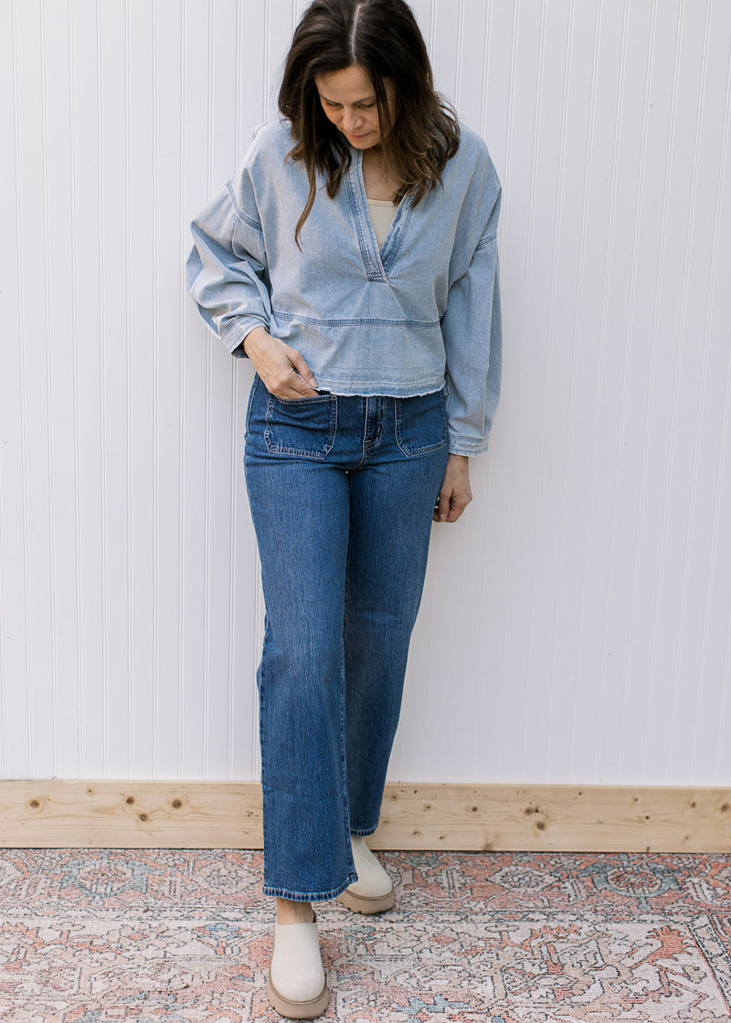 Model wearing a light denim top with a deep V, long sleeves and a raw hemline.