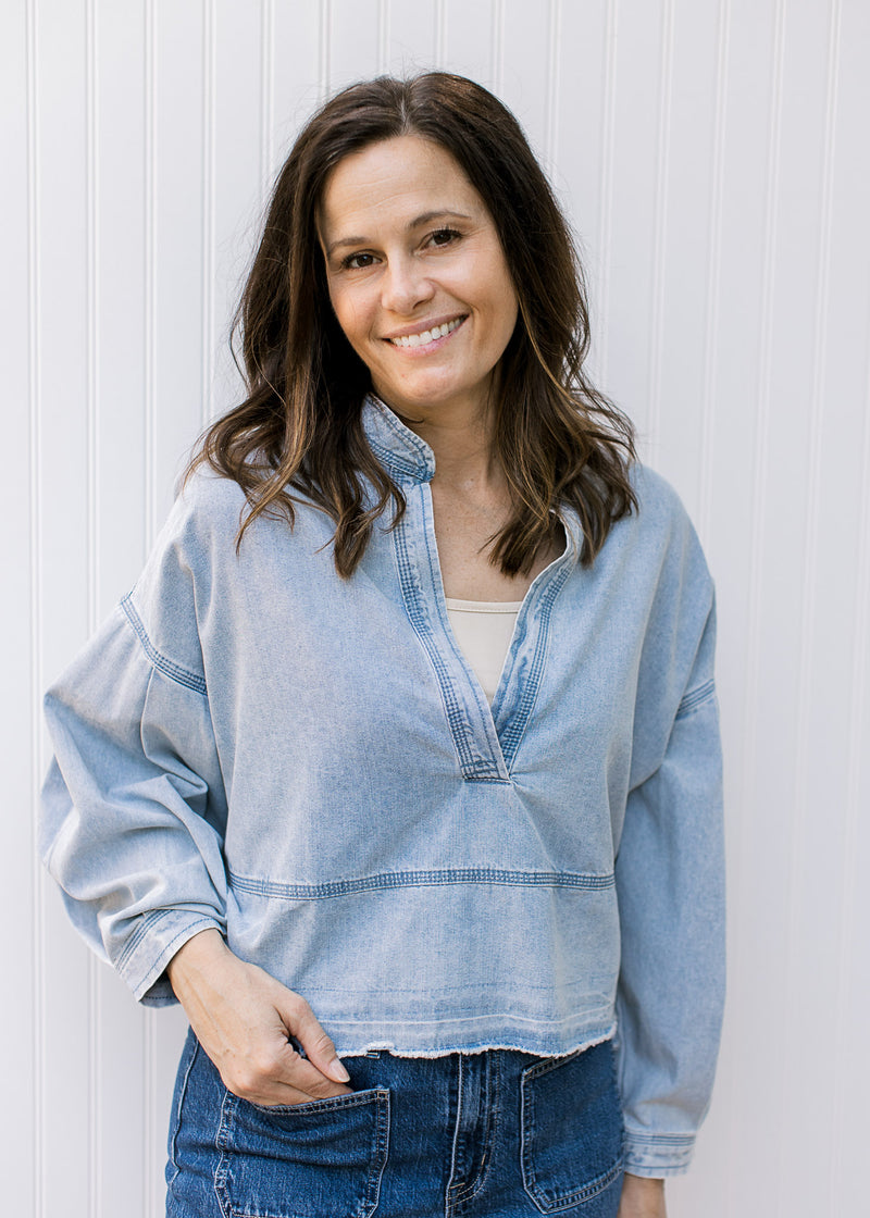 Model wearing a light denim top with extended shoulders, deep V neck and long sleeves.