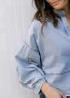 Close up of extended shoulder on a light denim top with long sleeves and deep V neck.