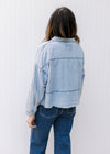 Back view of Model wearing a light denim top with a deep V, long sleeves and a raw hemline.