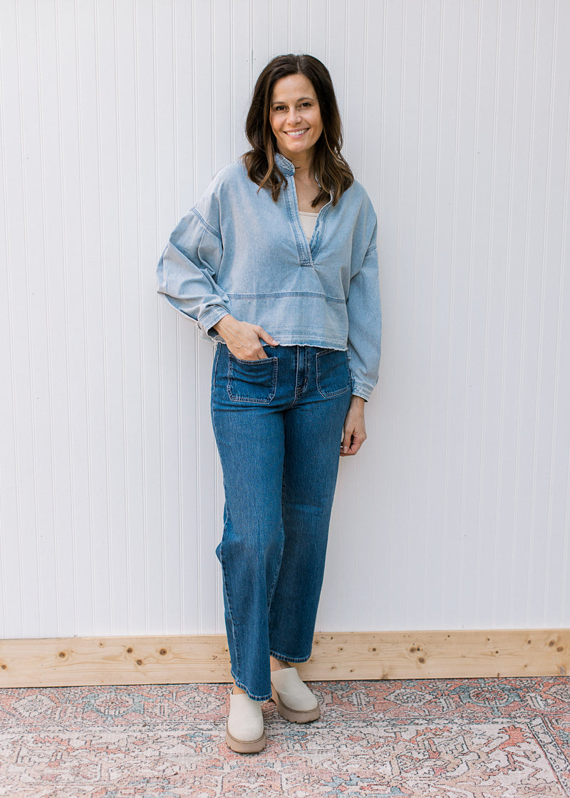 Model wearing jeans and mules with a light denim top with a deep V and long sleeves.