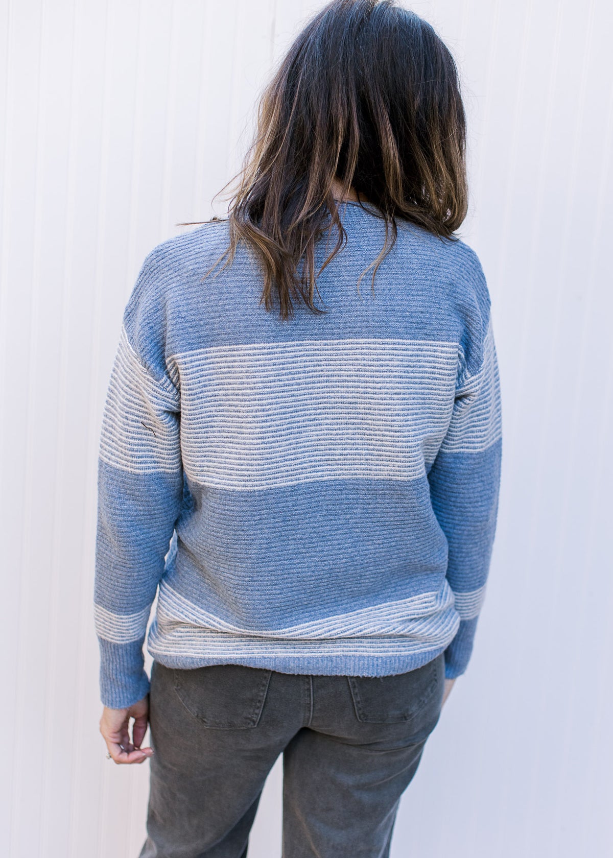 Back view of Model wearing a light blue and white color block, ribbed sweater with long sleeves. 