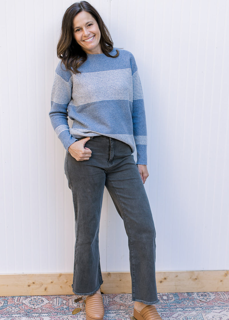 Model wearing jeans with a light blue and white ribbed sweater with long sleeves. 