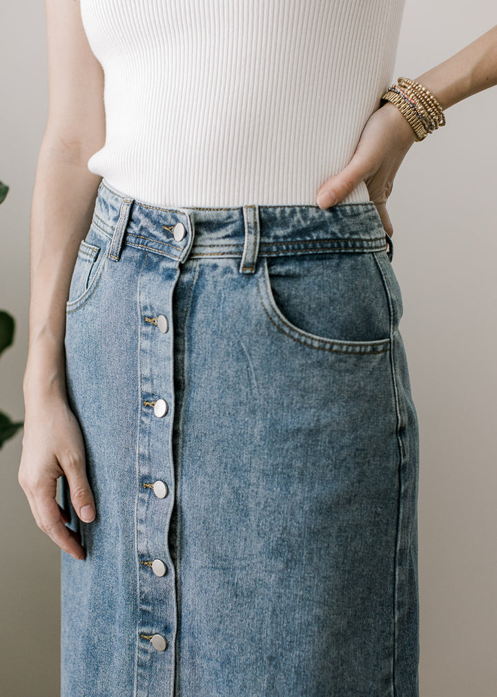 Close up of pockets, belt loops and button front on a medium wash denim maxi skirt. 