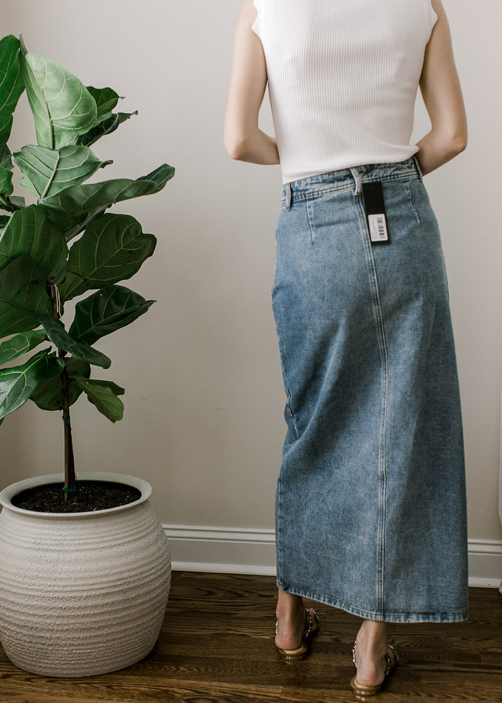 Back view of Model wearing a medium wash maxi denim skirt with button front and pockets. 