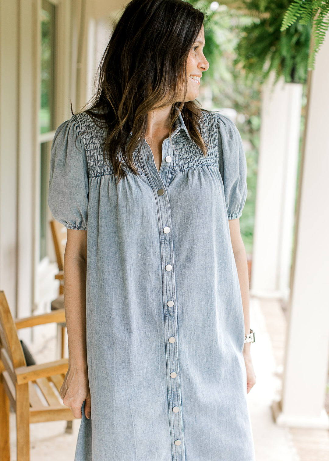 Model wearing a light wash denim dress with bubble short sleeves, v-neck  smocked yoke and buttons.