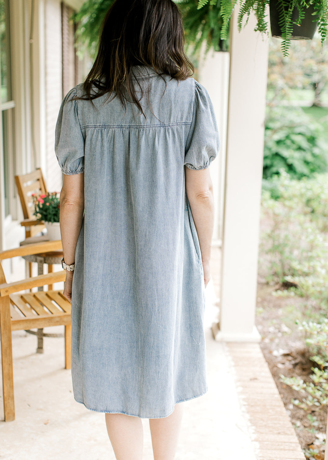 Back view of Model wearing a light wash denim dress with bubble short sleeves and a collar. 