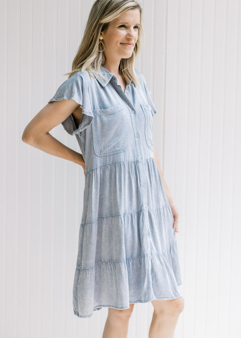 Model wearing a light denim button up dress with short sleeves, hitting above the knees. 
