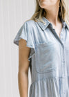 Close up of chest pockets and ruffle cap sleeve on a light denim above the knee dress. 