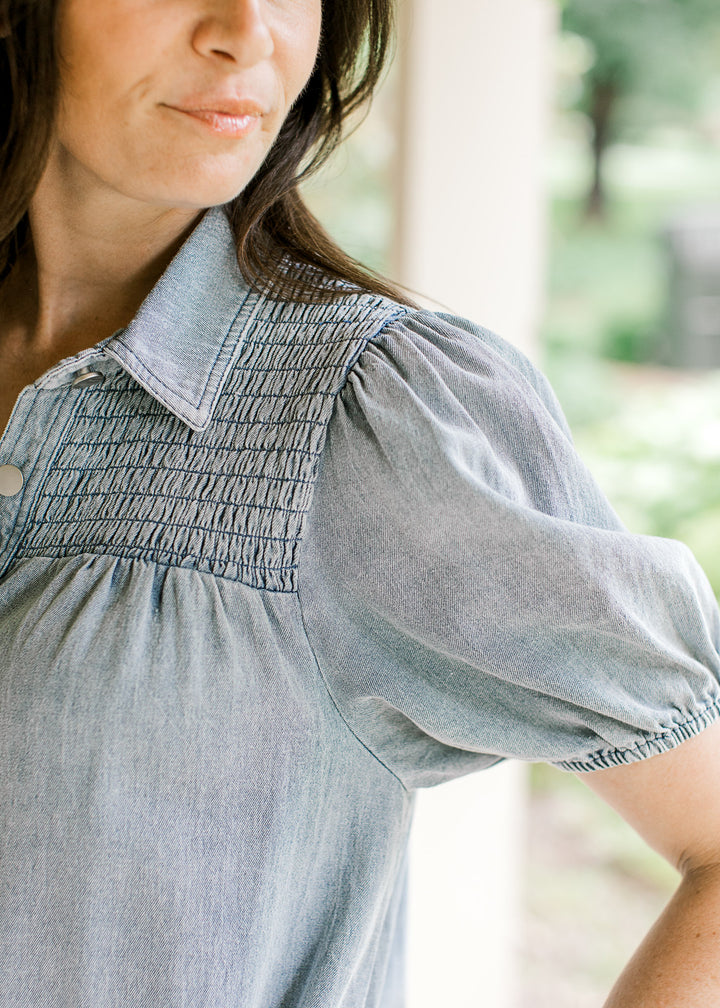 Close up of smocked yolk and collar on a light wash denim dress with bubble short sleeves. 