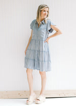 Model wearing wedges with a light denim button up dress with short sleeves, hitting above the knee. 