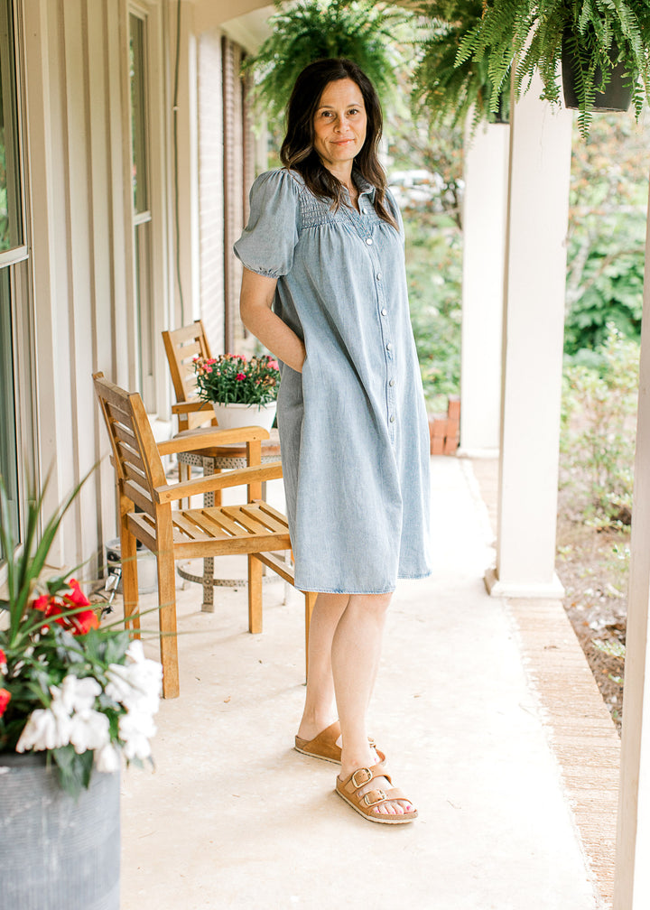 Model wearing sandals and a light denim dress with bubble short sleeves, smocked yoke and buttons.
