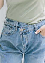 Close up view of criss cross button closure on waistband of medium washed jeans. 