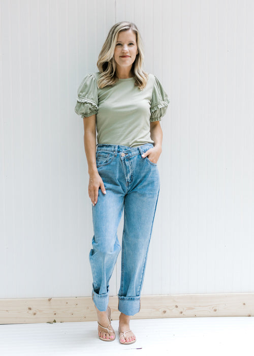 Model wearing a sage top with sandals and medium wash relaxed fit jeans with a criss cross waist.