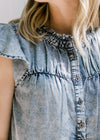 Close up view of flutter short sleeves and buttons on an acid washed denim top. 