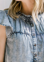 Close up view of flutter short sleeves and buttons on an acid washed denim top. 