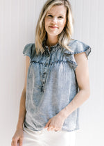 Blonde model wearing a acid washed denim top with flutter short sleeves and button front. 