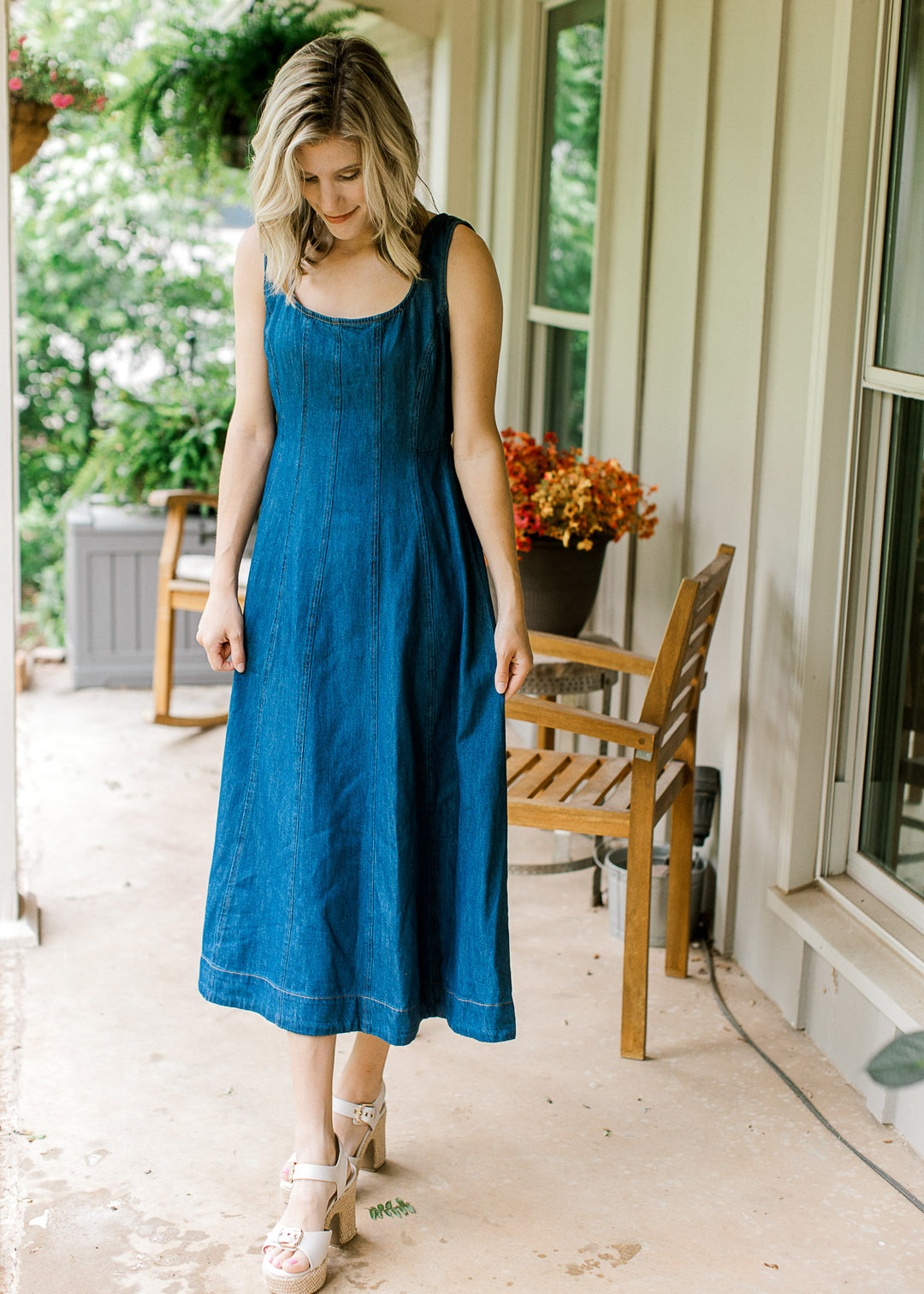 Model wearing wedges and a sleeveless dark denim midi with scoop neck and a panel design.