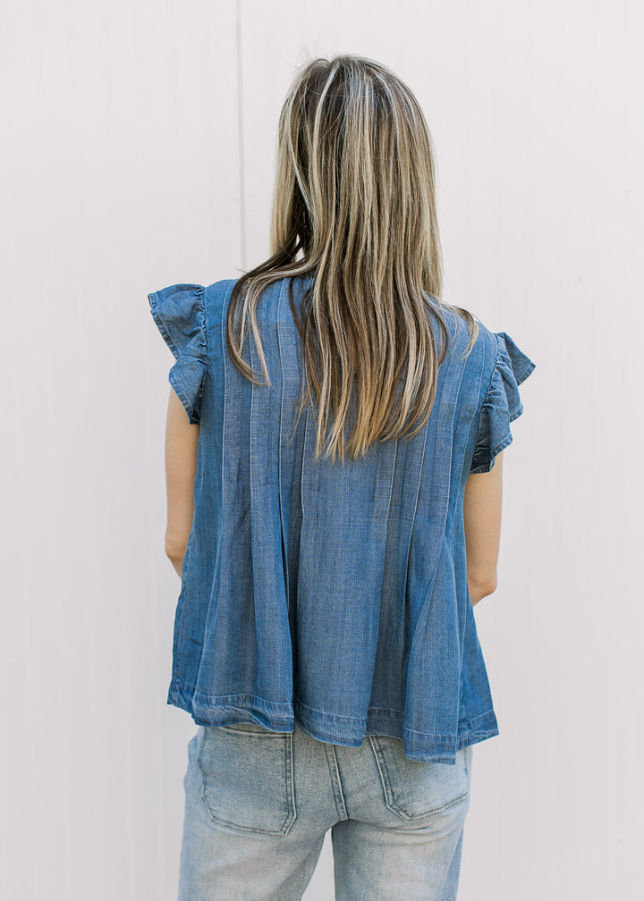 Back view of model wearing a medium/dark denim top with flutter cap sleeves and pleated design.