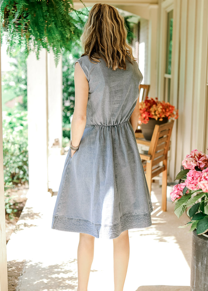 Back view of Model wearing a sleeveless light wash dress with elastic waist and pockets. 