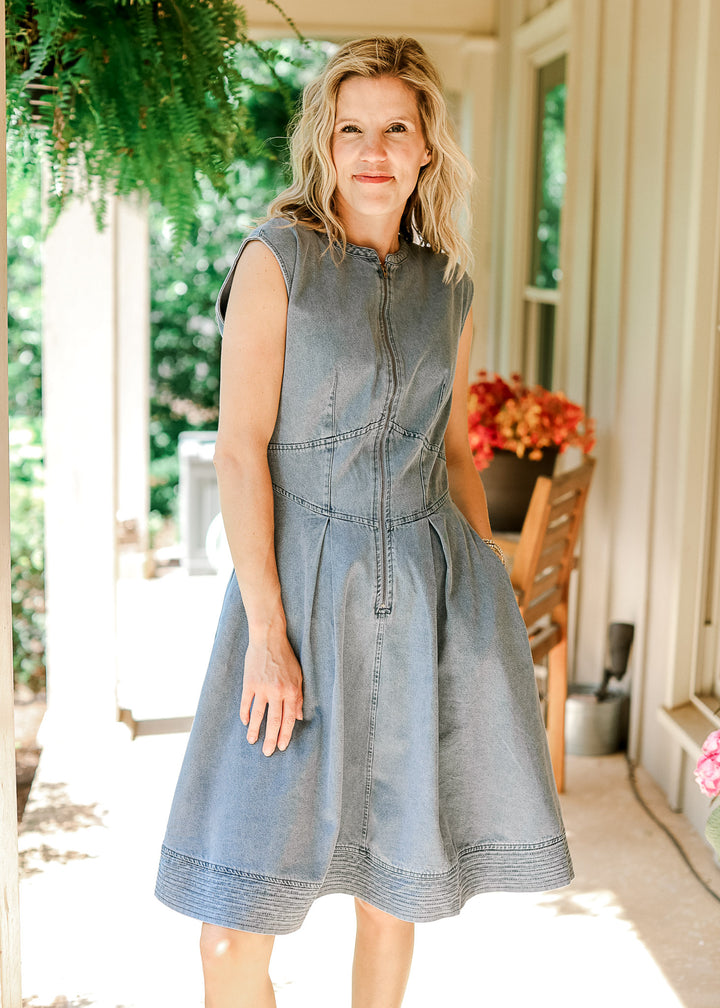 Model wearing a light wash sleeveless dress with a round neck, pockets and front zipper.