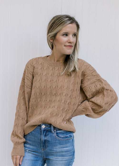 Model wearing a camel polyester sweater with a round neck, long sleeves and a cable knit fabric. 